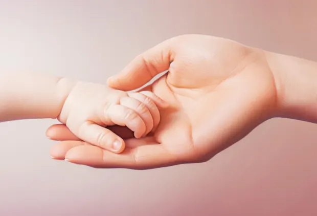 A newborn baby’s hand resting in an adult’s hand