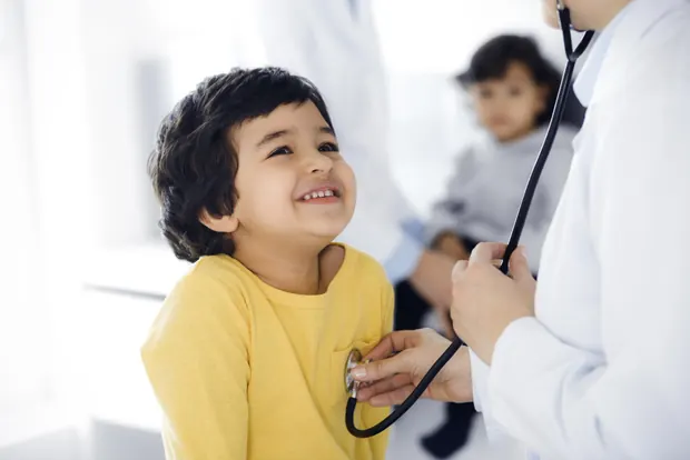 A doctor examining a smiling young child with a stethoscope during a consultation