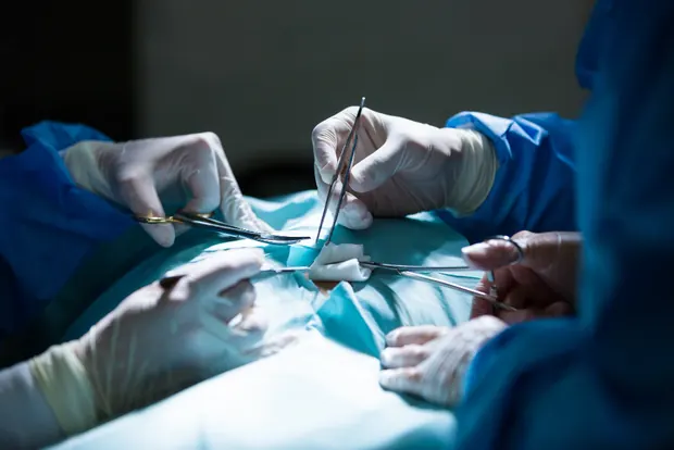 Surgical team working with instruments over a draped patient in an operating theatre
